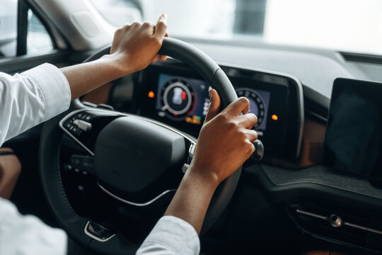 Two hands are on the steering wheel. Woman in white shirt is in the modern car
