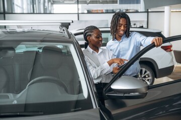 Documents in hands. Car seller is assisting client in the automobile salon