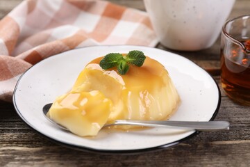 Delicious pudding with caramel sauce and mint served on wooden table, closeup