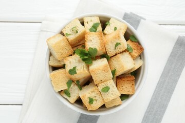 Delicious crispy croutons with parsley on white wooden table, top view