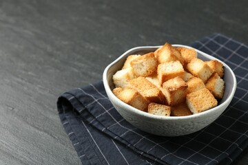 Tasty crispy croutons in bowl on dark textured table, closeup. Space for text