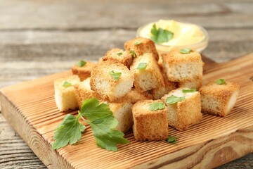 Tasty crispy croutons with cut parsley and sauce on wooden table, closeup