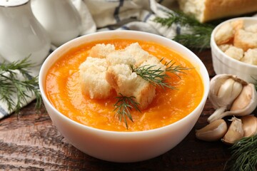 Delicious pumpkin cream soup with croutons, dill and ingredients on wooden table, closeup