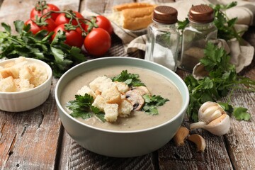 Delicious mushroom cream soup with croutons and ingredients on wooden table, closeup