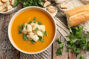Tasty pumpkin cream soup with croutons and parsley in bowl on wooden table, flat lay