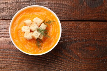Delicious pumpkin cream soup with croutons and dill in bowl on wooden table, top view. Space for text
