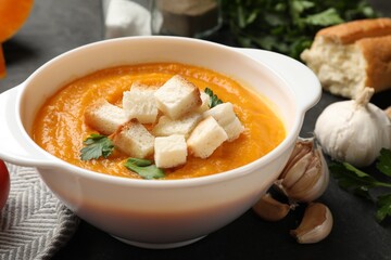 Tasty pumpkin cream soup with croutons, parsley and garlic on dark table, closeup