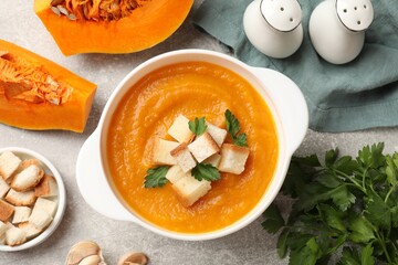 Tasty pumpkin cream soup with croutons and parsley in bowl on grey textured table, flat lay