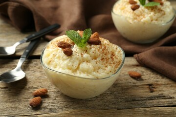 Delicious rice pudding with cinnamon, almonds and mint served on wooden table, closeup