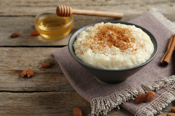 Delicious rice pudding with cinnamon, honey and almonds on wooden table, closeup