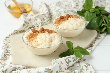 Delicious rice pudding with cinnamon, almonds, honey and mint on white wooden table, closeup
