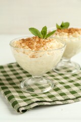 Delicious rice pudding with cinnamon and mint in glass dessert bowls on white wooden table, closeup