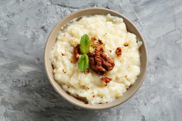Delicious rice pudding with walnuts and mint on grey table, top view