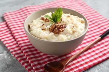 Delicious rice pudding with walnuts, mint and spoon on grey table, closeup