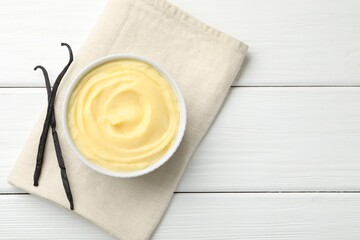 Tasty vanilla pudding and pods on white wooden table, top view. Space for text