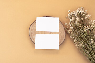 White blank business card mockup with dried flower on brown background