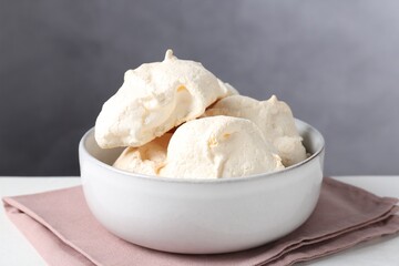 Delicious homemade meringue cookies in bowl on light table against gray background, closeup