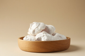 Delicious homemade meringue cookies in bowl on beige background