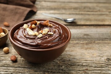 Delicious chocolate pudding with nuts in bowl on wooden table, closeup. Space for text