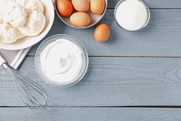 Delicious homemade meringue cookies, ingredients and whisk on gray wooden table, flat lay. Space for text