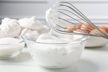 Whisk with whipped cream and other ingredients on light table, closeup. Cooking meringue cookies