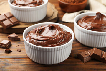 Tasty pudding in bowls and pieces of chocolate on wooden table, closeup