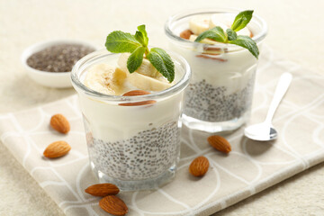 Delicious dessert with chia seeds, yogurt, banana, almond and mint in glasses on light textured table, closeup. Superfood