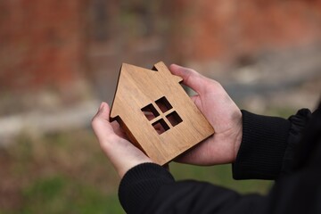 Homeless man with wooden house figure outdoors, closeup