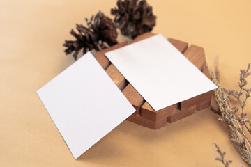 White blank business card mockup with wooden coaster and dried flower on brown background