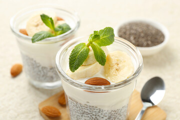 Delicious dessert with chia seeds, yogurt, banana, almond and mint in glasses on light table, closeup. Superfood