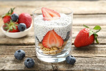 Delicious dessert with chia seeds, yogurt, granola, strawberries and blueberries in glass on wooden table, closeup. Superfood