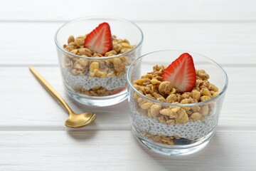 Delicious dessert with chia seeds, yogurt, granola and strawberries in glasses on white wooden table, closeup. Superfood