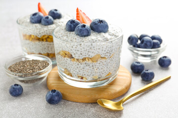 Delicious pudding with chia seeds, yogurt, blueberries, granola and strawberry on light grey table, closeup. Superfood