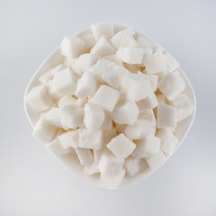 White plate with pieces of crushed white sugar on a white background, top view. Sugar in pieces.