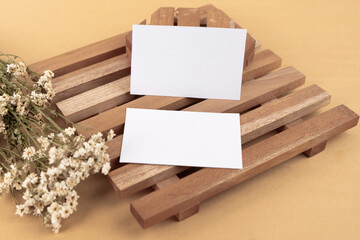 White blank business card mockup with wooden decoration and dried flower on brown background
