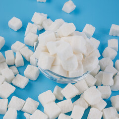 White sugar in a glass cup, scattered lump sugar on a blue background. Top view.