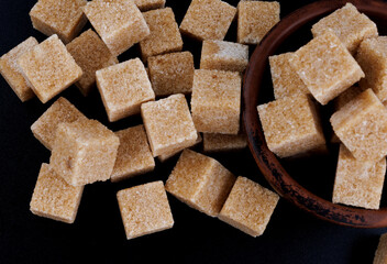 Clay cup with sugar cubes on black background. Cane brown sugar.