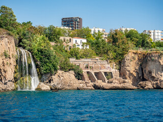 Waterfall and ancient ruins. Sea and rocks in Antalya, Turkey. A magical fairy-tale landscape. A ship is sailing against the background of the mountains.