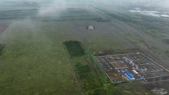 Bird's-eye view of power lines, a green field and trees