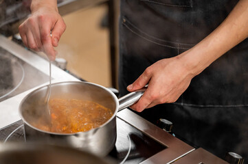 A close-up of a chef's hand stirring a simmering pot of stew on the stovetop, with steam rising, showcasing the cooking process in a professional kitchen.