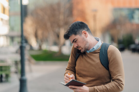 Businessman writing notes while talking on phone in urban setting