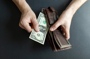 man takes out the last 1 dollar bill from his wallet. abstraction on the topic of high cost of living and bankruptcy