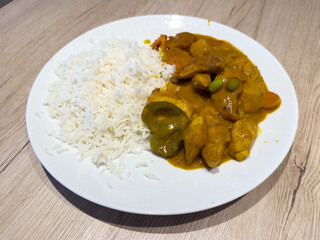 Plate of curry chicken with rice on wooden table