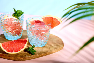 A chilled summer cocktail or drink with fresh grapefruit slices and ice cubes under palm leaves. Refreshing citrus soda