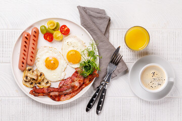 A classic breakfast plate featuring sunny-side-up eggs, crispy bacon, sausages, and fresh tomatoes