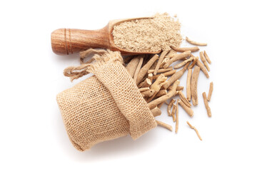 A scoop of organic Ashwagandha (Withania somnifera) powder, along with ashwagandha roots spilled out from a jute bag. Isolated on a white background.
