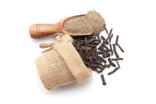 A scoop of organic long pepper (Piper longum) powder, along with long pepper fruits spilled out from a jute bag. Isolated on a white background.