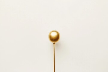 A single gold-painted spoon with a round bowl, elegantly positioned against a minimalist white background.