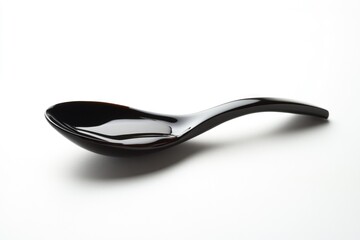 A sleek, black spoon, possibly made of resin, rests on a white background, containing a dark liquid.
