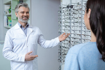 Female patient consulting optometrist in shop while selecting eyewear for sight correction